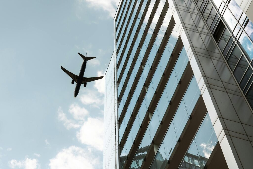 Airplane soaring above a modern glass skyscraper with a bright sky backdrop.